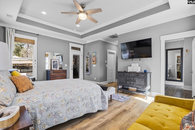 bedroom with baseboards, visible vents, a raised ceiling, and wood finished floors