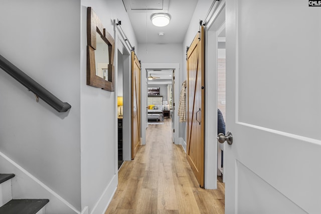 hall featuring light wood-style flooring, a barn door, attic access, baseboards, and stairs