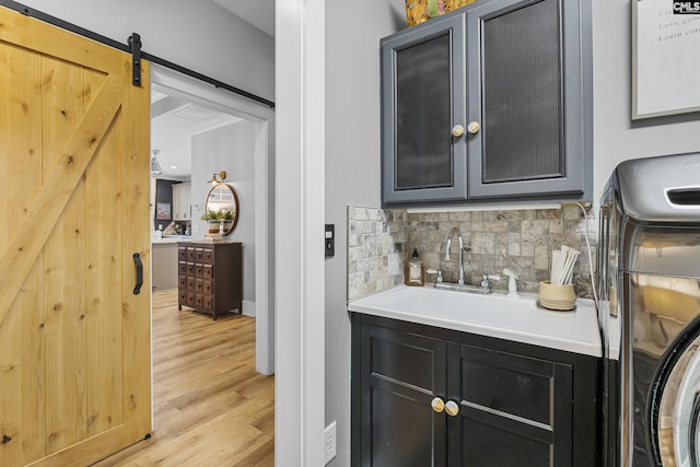 bar with a barn door, a sink, light wood-type flooring, decorative backsplash, and washer / clothes dryer