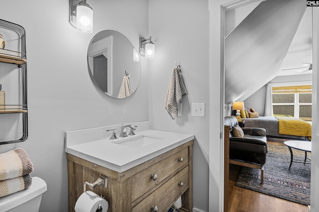 half bathroom with toilet, lofted ceiling, wood finished floors, and vanity