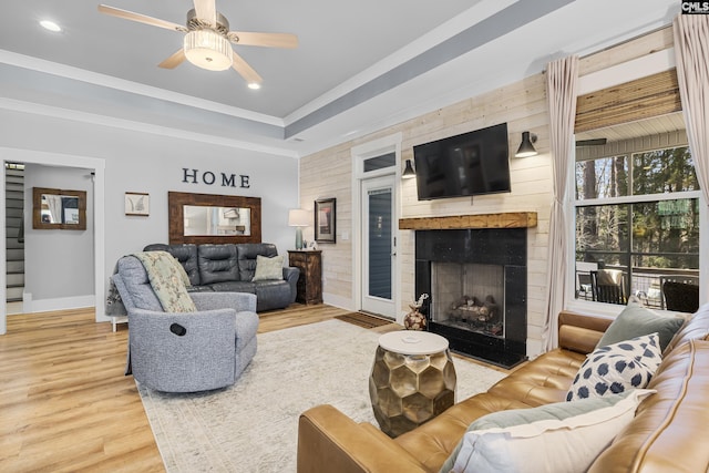 living area with a raised ceiling, a large fireplace, ceiling fan, wood finished floors, and baseboards