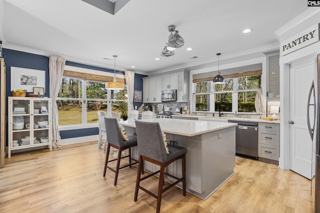 kitchen featuring light wood finished floors, light countertops, gray cabinetry, appliances with stainless steel finishes, and a kitchen island