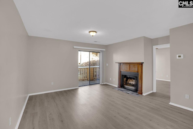 unfurnished living room featuring a fireplace with flush hearth, baseboards, and wood finished floors