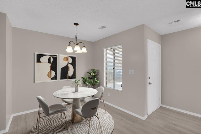 dining space with a chandelier, baseboards, visible vents, and light wood finished floors