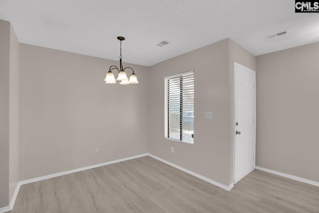 spare room with light wood-style floors, visible vents, a notable chandelier, and baseboards