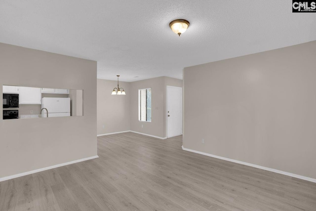 unfurnished living room with light wood-style floors, baseboards, a chandelier, and a textured ceiling