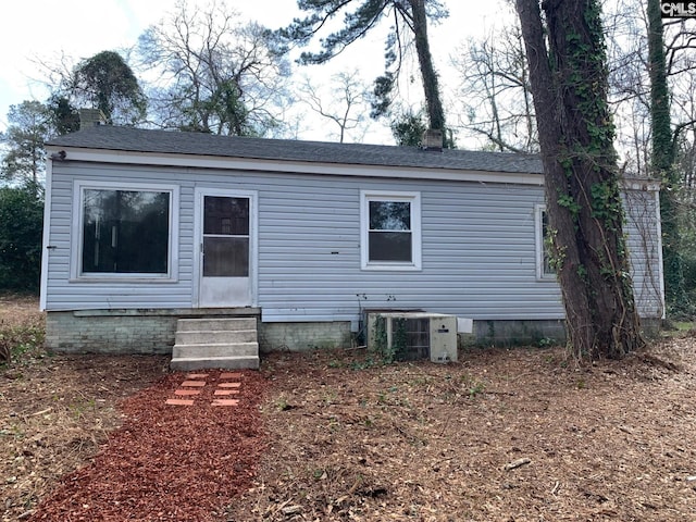 rear view of property featuring entry steps, central AC unit, and a chimney