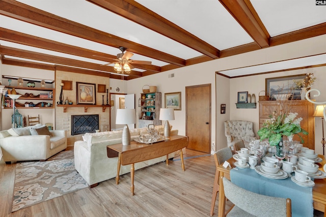 living area with a ceiling fan, a fireplace, beam ceiling, and wood finished floors