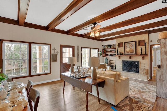 living area with beam ceiling, a fireplace, ceiling fan, wood finished floors, and baseboards