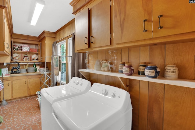 clothes washing area with wood walls, washing machine and clothes dryer, and cabinet space