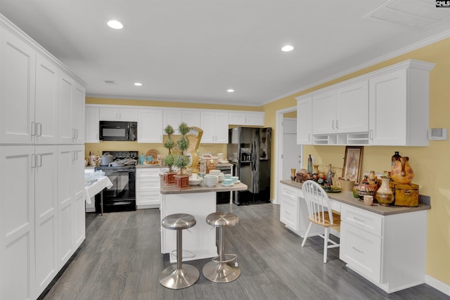 kitchen with a breakfast bar, white cabinetry, black appliances, and wood finished floors