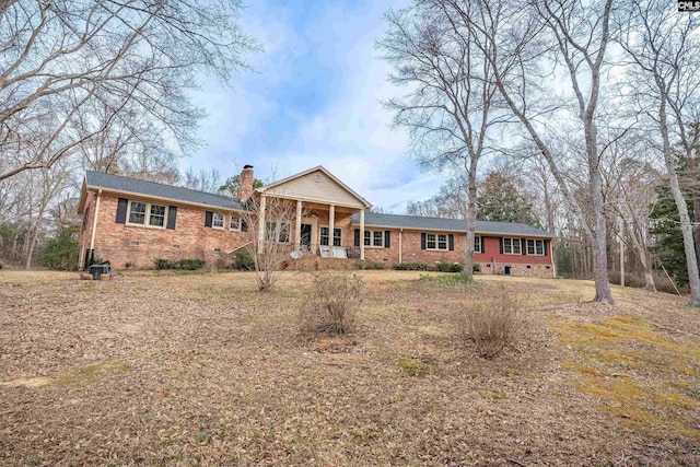 view of front facade with a porch, brick siding, crawl space, and a chimney