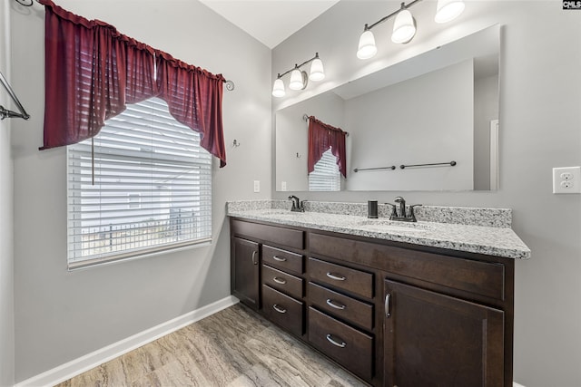 bathroom featuring wood finished floors, a sink, baseboards, and double vanity