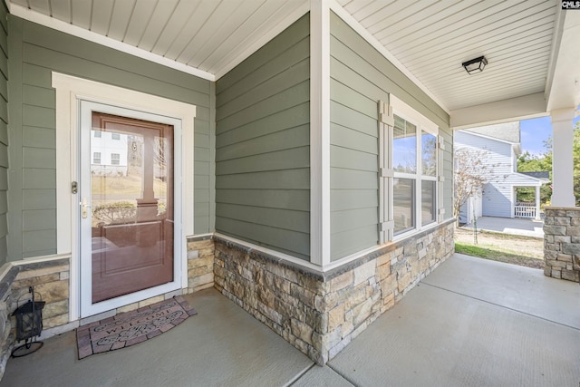 view of exterior entry featuring stone siding and covered porch