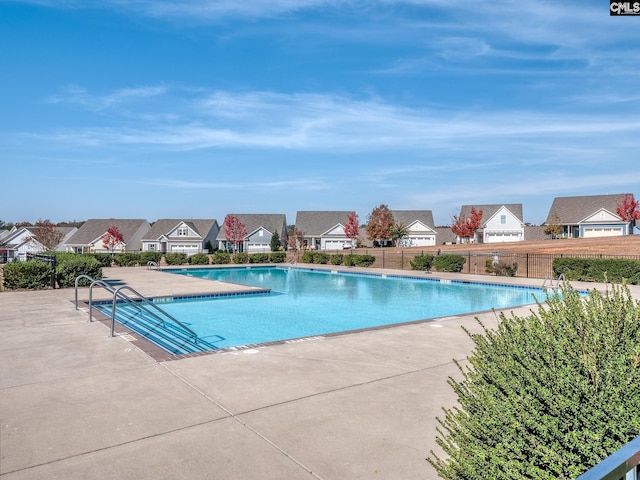 pool with a patio area, fence, and a residential view