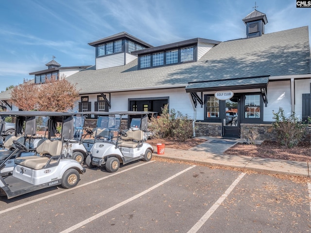 exterior space featuring a shingled roof, stone siding, and uncovered parking