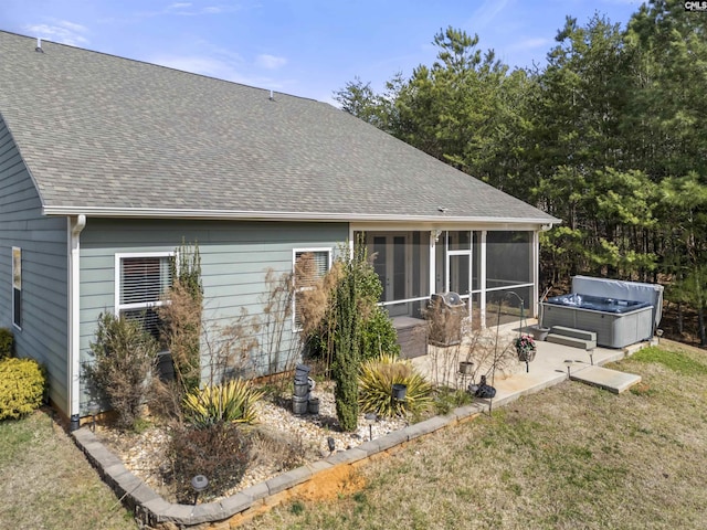 rear view of property featuring roof with shingles, a lawn, a hot tub, a sunroom, and a patio area