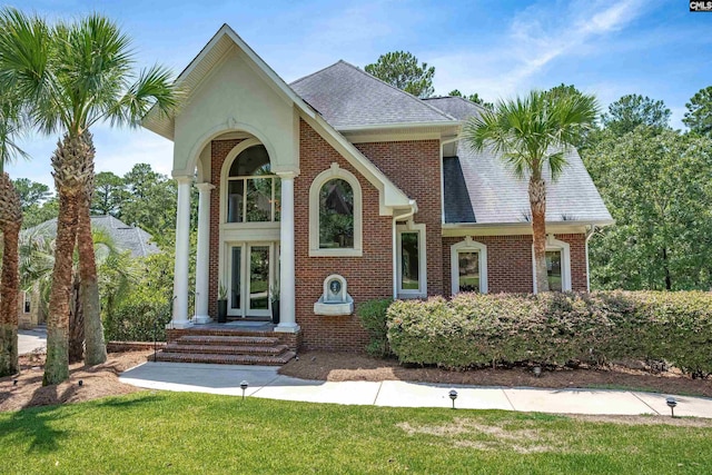 view of front facade with brick siding, a shingled roof, and a front yard