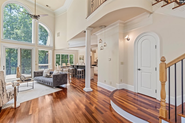 living area with ornate columns, stairs, a ceiling fan, and wood finished floors