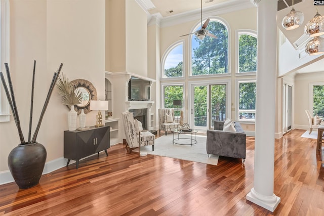 living area featuring ceiling fan, a fireplace, ornamental molding, wood-type flooring, and ornate columns