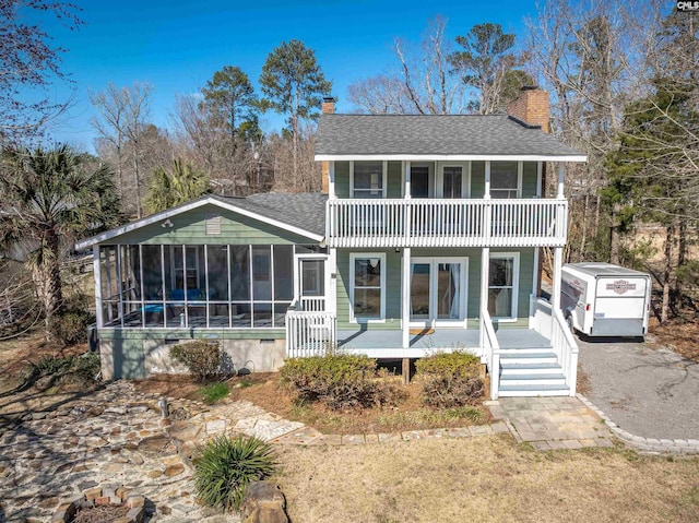 rear view of house featuring a porch, a balcony, a sunroom, roof with shingles, and a chimney