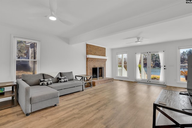 living room with beamed ceiling, a brick fireplace, wood finished floors, and a ceiling fan