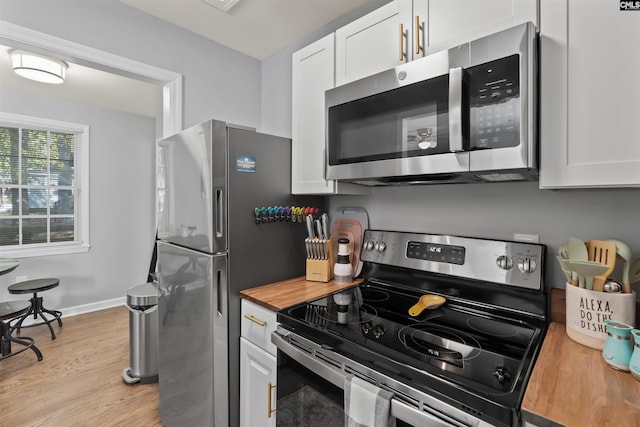 kitchen with appliances with stainless steel finishes, butcher block countertops, light wood-style flooring, and white cabinetry