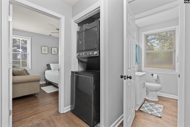 ensuite bathroom featuring a healthy amount of sunlight, stacked washer / dryer, and wood finished floors