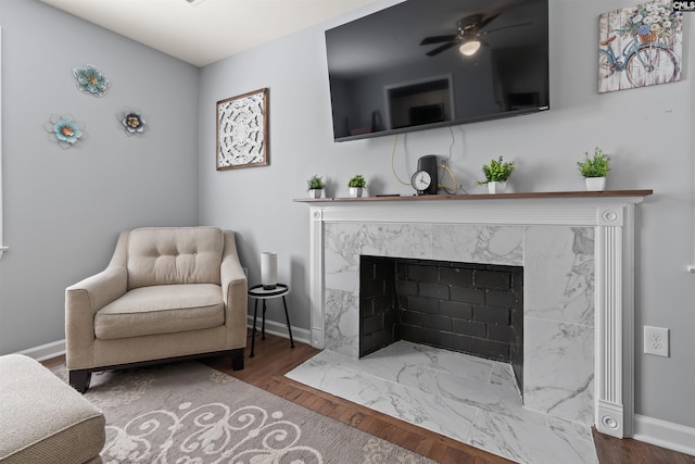 living area featuring ceiling fan, a premium fireplace, wood finished floors, and baseboards