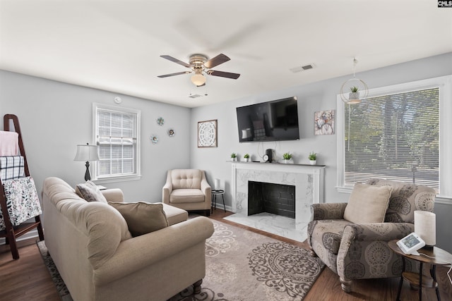 living area with a ceiling fan, a high end fireplace, visible vents, and wood finished floors