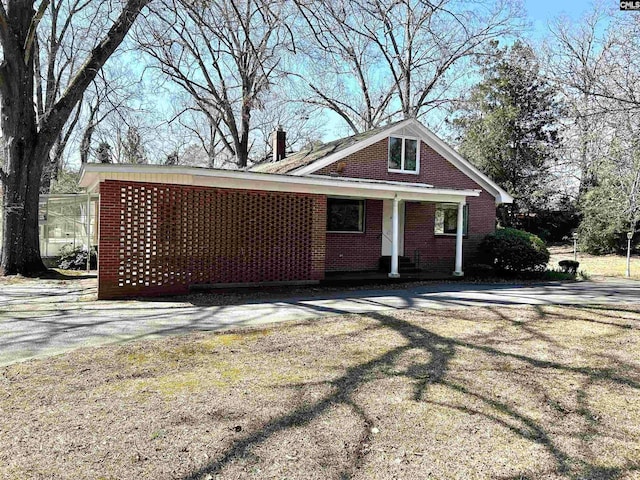 view of front facade with driveway, brick siding, and a chimney