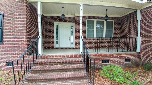 doorway to property featuring crawl space, covered porch, and brick siding