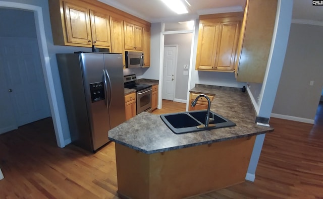 kitchen featuring light wood finished floors, dark countertops, a peninsula, stainless steel appliances, and a sink