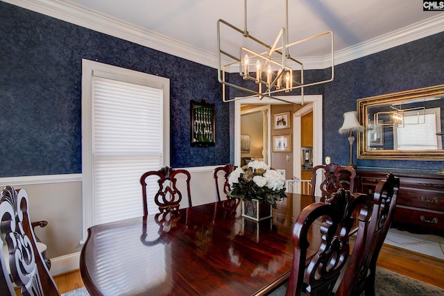 dining room with wallpapered walls, a wainscoted wall, ornamental molding, wood finished floors, and an inviting chandelier