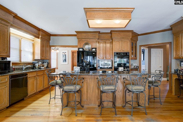 kitchen featuring a large island, light wood-style flooring, a breakfast bar, crown molding, and black appliances