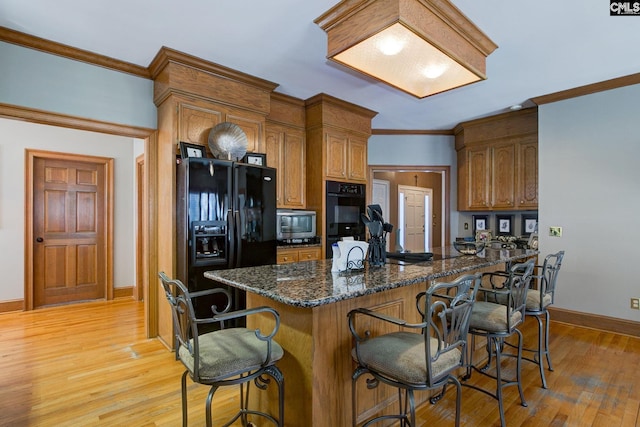 kitchen featuring black appliances, ornamental molding, a breakfast bar, and light wood-style floors