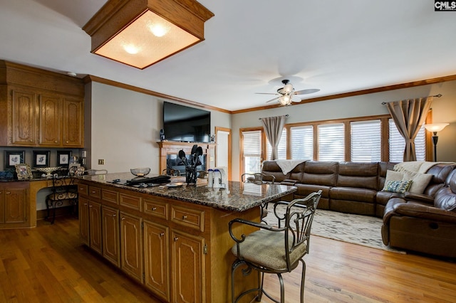 kitchen featuring open floor plan, light wood finished floors, ornamental molding, a center island, and built in desk