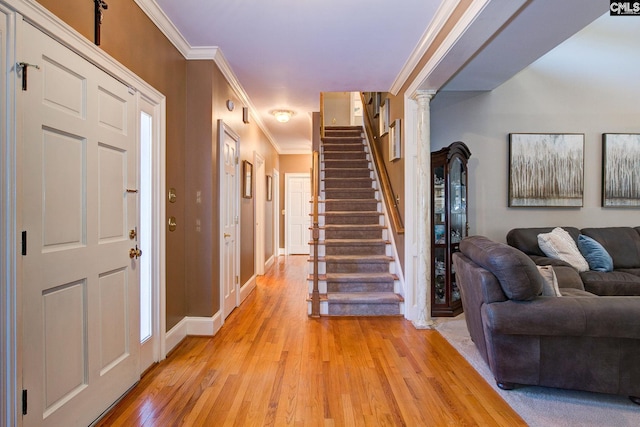 entrance foyer with ornate columns, stairway, ornamental molding, light wood-type flooring, and baseboards