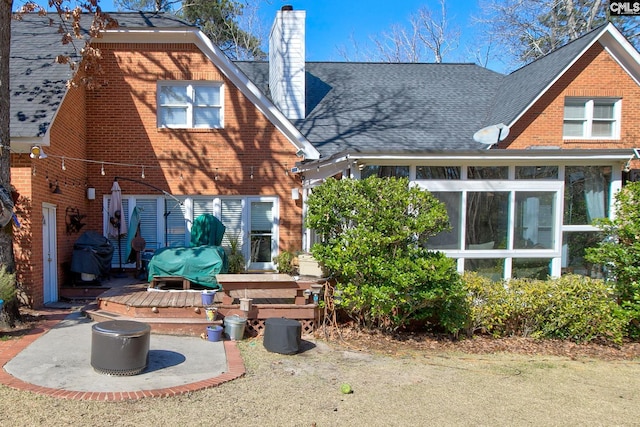 back of property with a sunroom, a chimney, roof with shingles, a deck, and brick siding