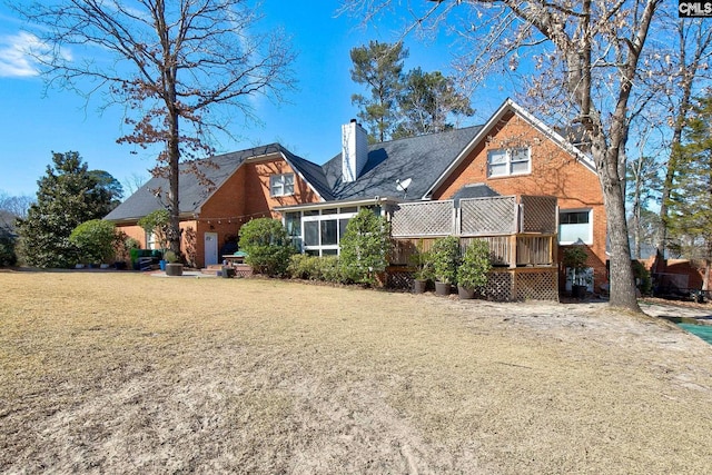 rear view of house featuring a chimney, a deck, a lawn, and brick siding