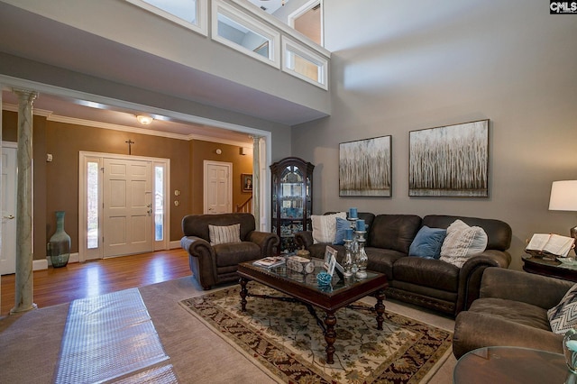 living room with decorative columns, crown molding, a towering ceiling, wood finished floors, and baseboards