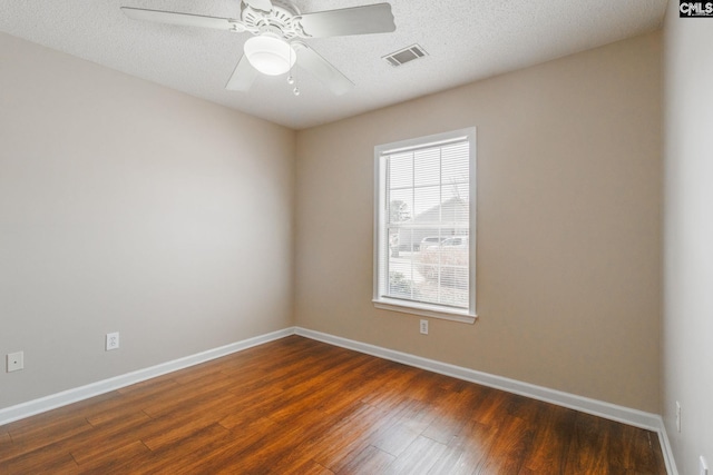 empty room with a textured ceiling, a ceiling fan, visible vents, baseboards, and dark wood finished floors