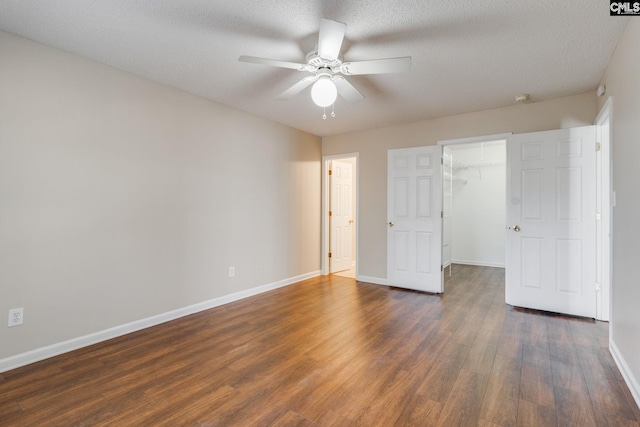 unfurnished bedroom featuring a textured ceiling, baseboards, a walk in closet, and dark wood-type flooring