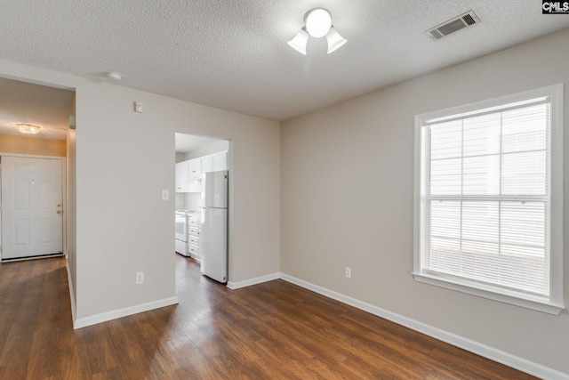 unfurnished room featuring a textured ceiling, dark wood-style flooring, visible vents, and baseboards