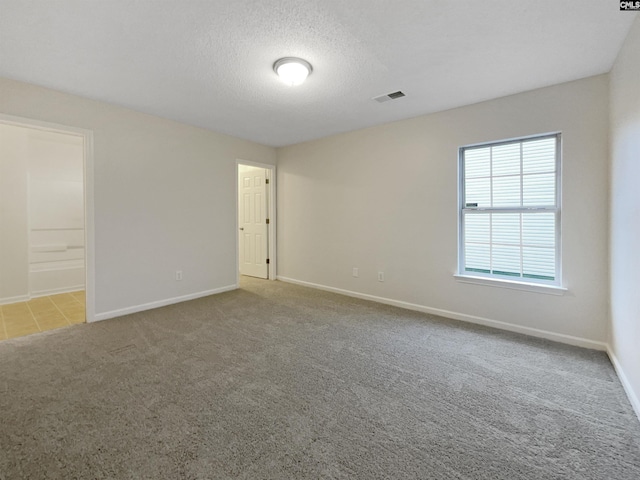 empty room featuring a textured ceiling, carpet flooring, visible vents, and baseboards