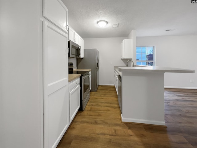 kitchen with a peninsula, white cabinetry, appliances with stainless steel finishes, and dark wood-type flooring