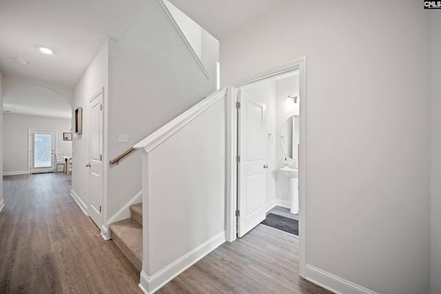 hallway featuring arched walkways, wood finished floors, stairs, and baseboards