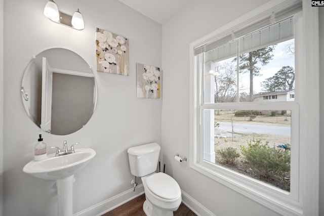 half bath with toilet, baseboards, and wood finished floors