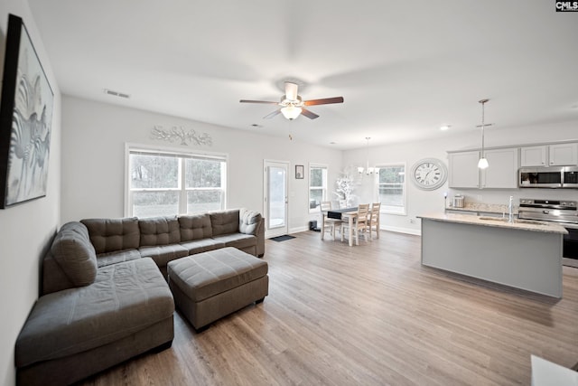 living area featuring a ceiling fan, baseboards, visible vents, and light wood finished floors