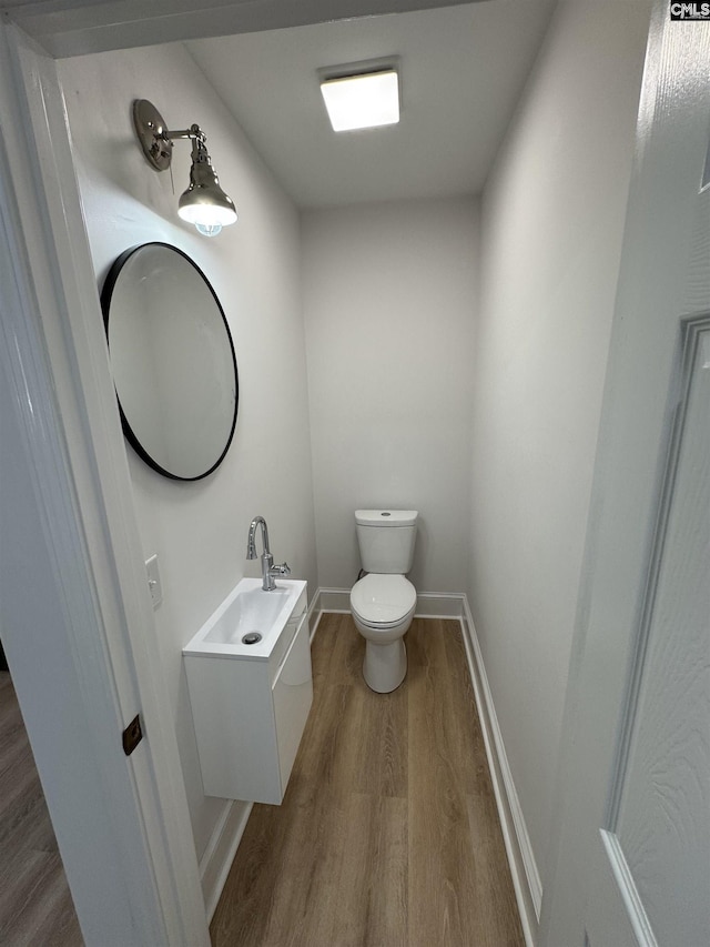 bathroom featuring toilet, baseboards, wood finished floors, and vanity